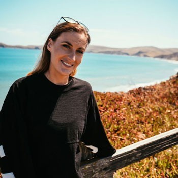 Casey, Ads Team Director at Elevate Her Marketing, smiles at the camera in front of the ocean