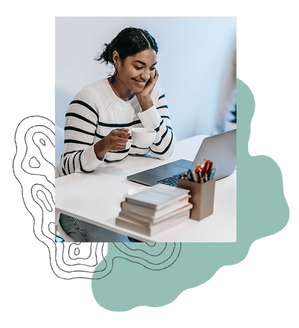 Woman smiles at her laptop while drinking coffee