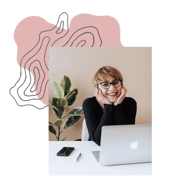 Woman smiles at the camera with her elbows on the table with her laptop open in front of her