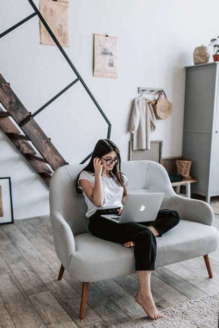 A girl sits on a couch smiling with a laptop