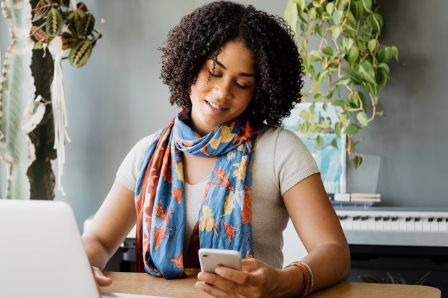 Woman sitting at a table, smiling and viewing content on a smartphone such as Facebook ads or posts