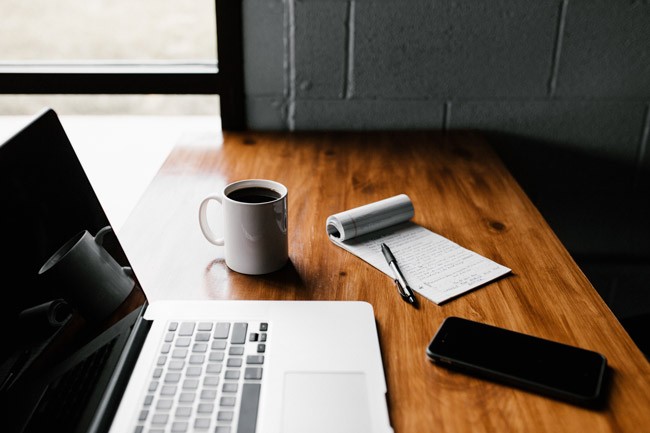 Laptop on a wooden table with coffee cup next to a paper Facebook and Instagram marketing checklist"