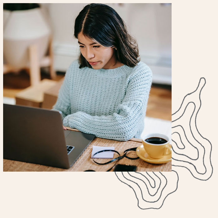 Woman smiles at her computer while drinking coffee