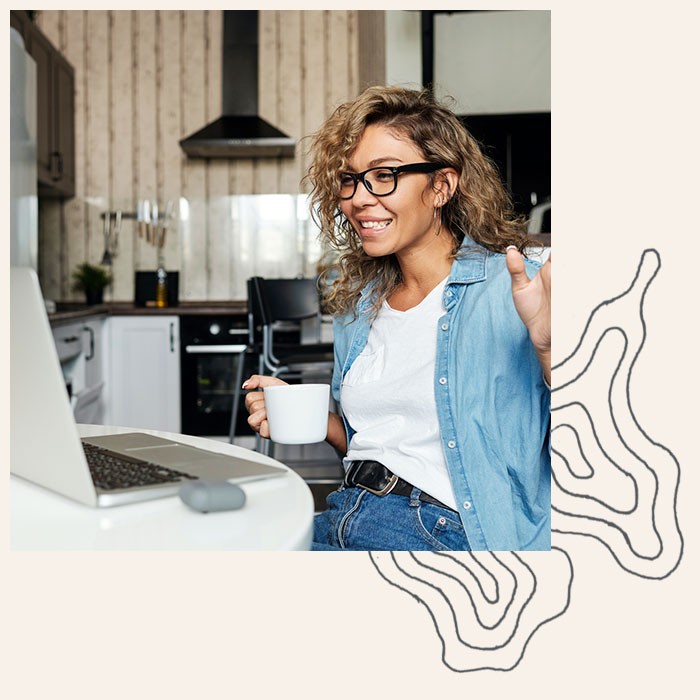 Woman smiles at her computer while drinking coffee
