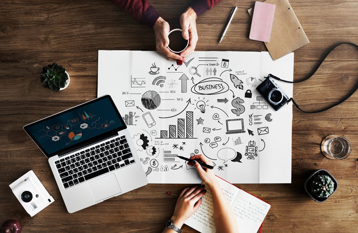 Top view of a laptop and the hands of a man and woman whiteboarding (on paper) a digital marketing ecosystem